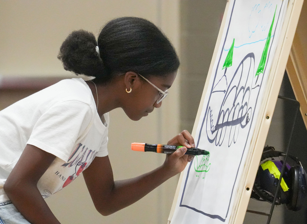 A person uses a marker to write on a large whiteboard, focusing on a green drawing.