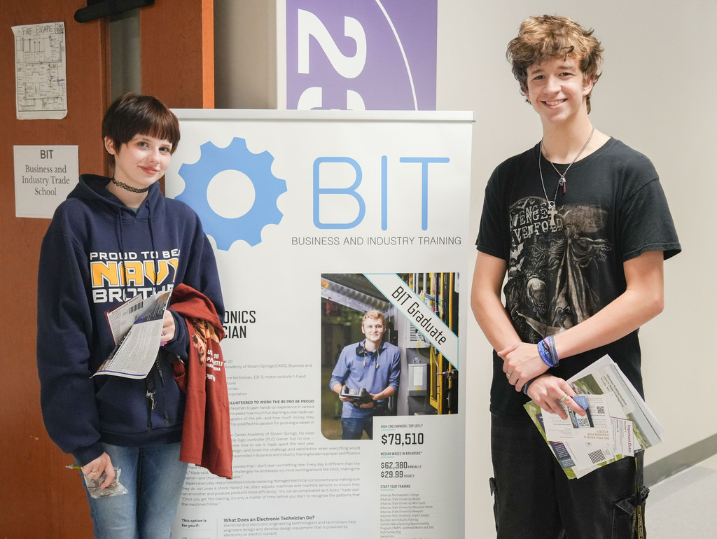 Two students, one with a hoodie and the other in a T-shirt, standing beside a poster with the acronym BIT.