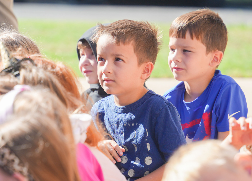 A group of children outside, some with hoodies, one with a blue shirt and red stripe.