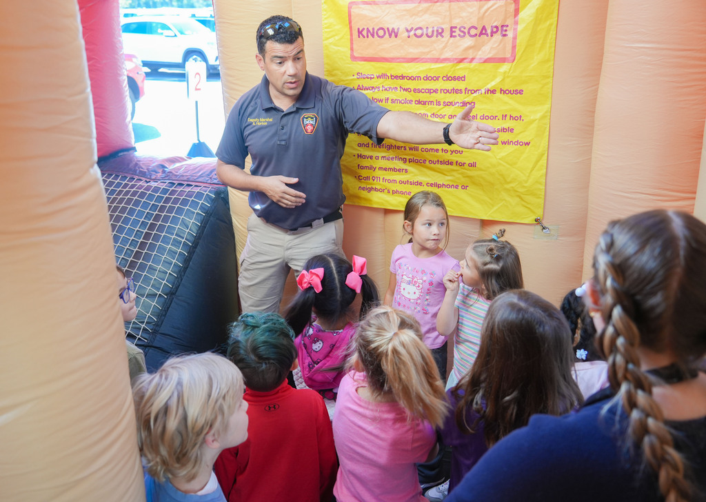 A man talks to a group of children in a bounce house, wearing a blue shirt.