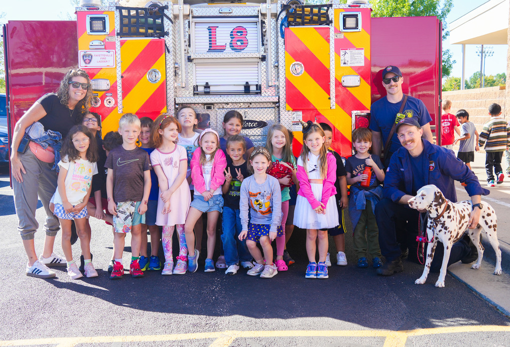 Group of children in various outfits, two adults, and a dog posing in front of a fire truck.