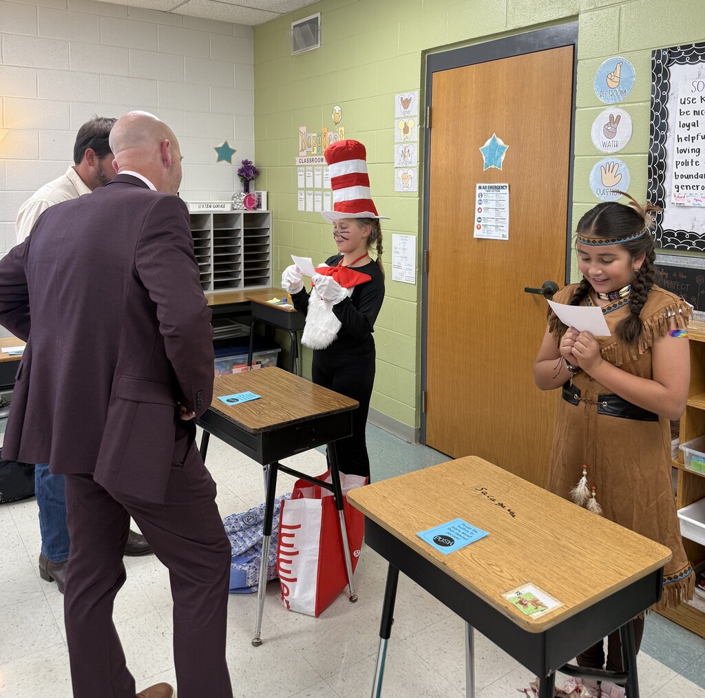 Man in a suit standing with a young girl holding a paper. A young girl in a Cat in the Hat costume.