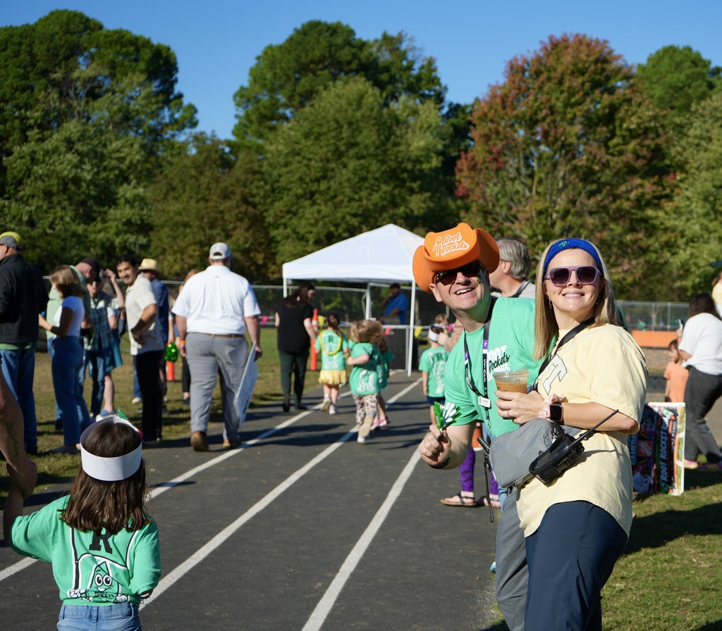 A group of people on a track, some in matching shirts, stand near a tent. Trees in the background.