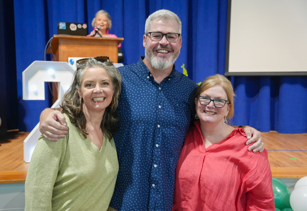 Three smiling adults on stage with a large white number 2 behind them.