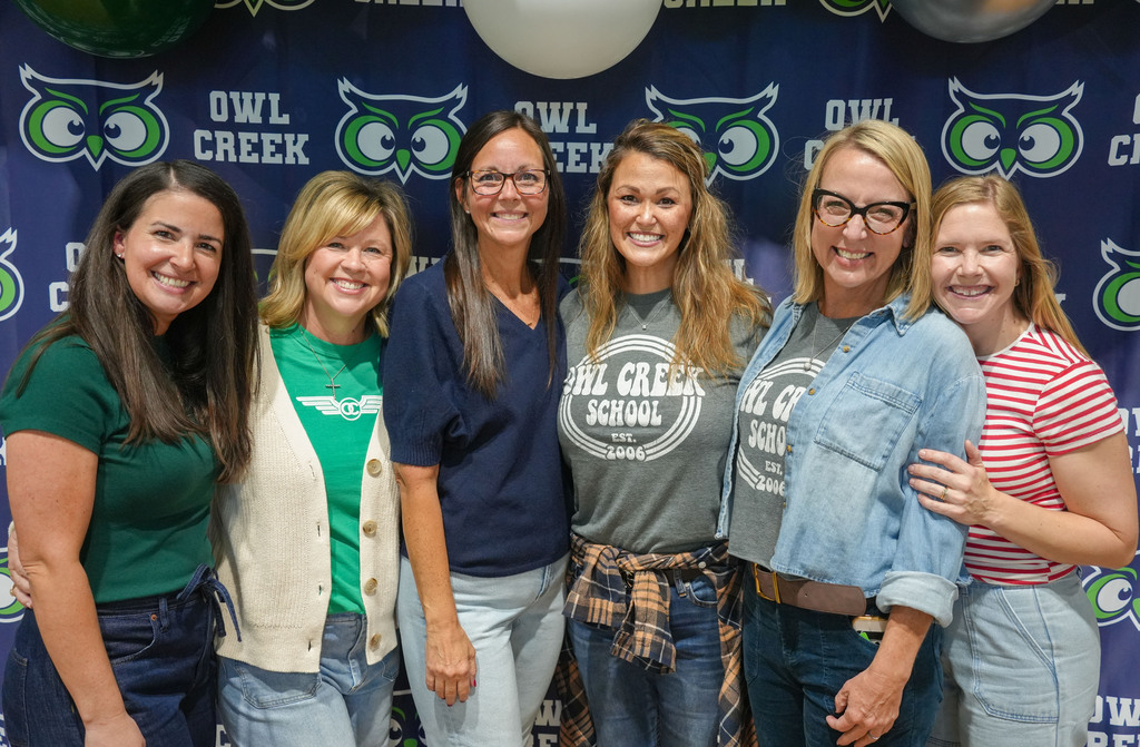 Six women pose for a photo in front of a blue backdrop with a logo.