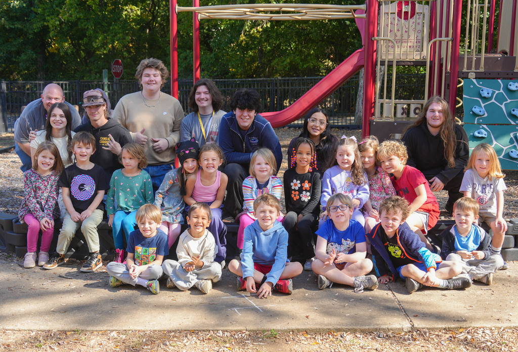 A group of children and adults posing outside by a playground.