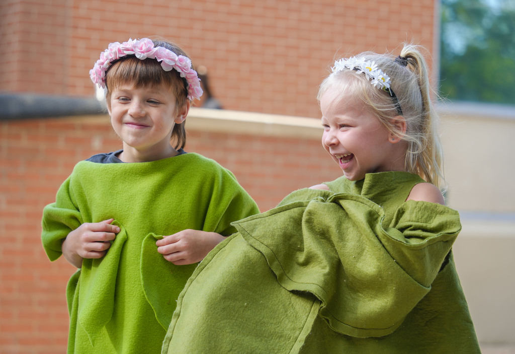 Two children wearing green hooded towels, standing outside next to a brick wall.