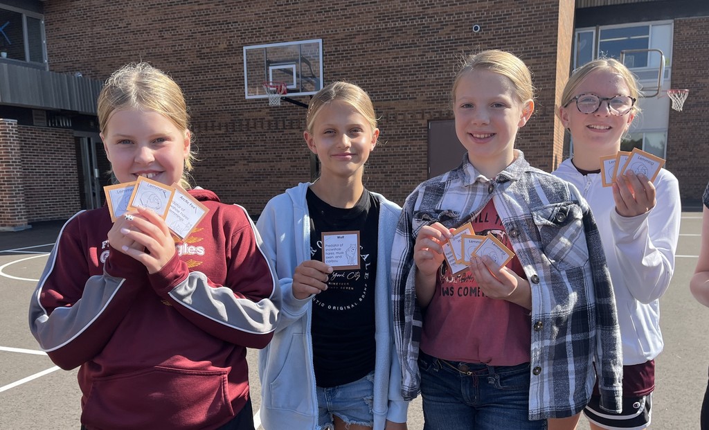 a student show off the cards they collected in the predator play game outside