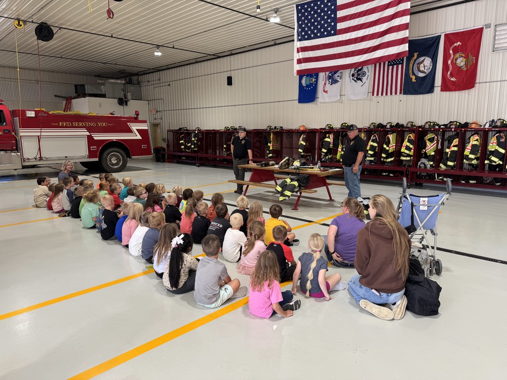 students sit at the fire station on the floor and listen to the fire fighter