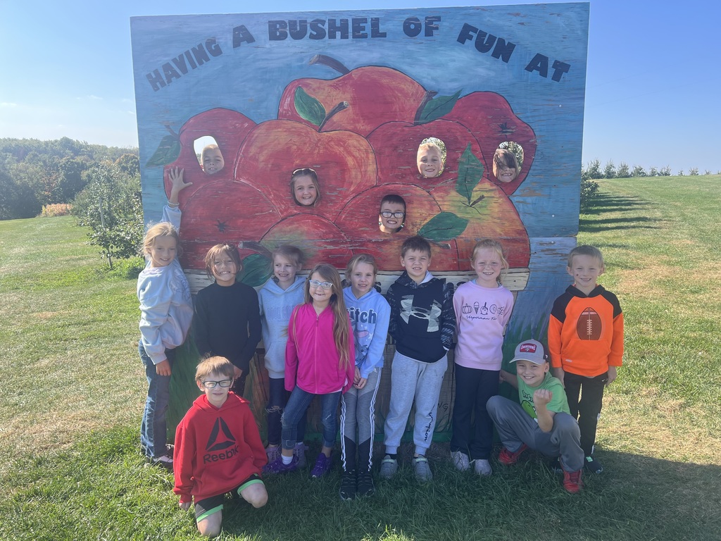2nd grade pose in front of a picture that says having a bushel of fun at the orchard