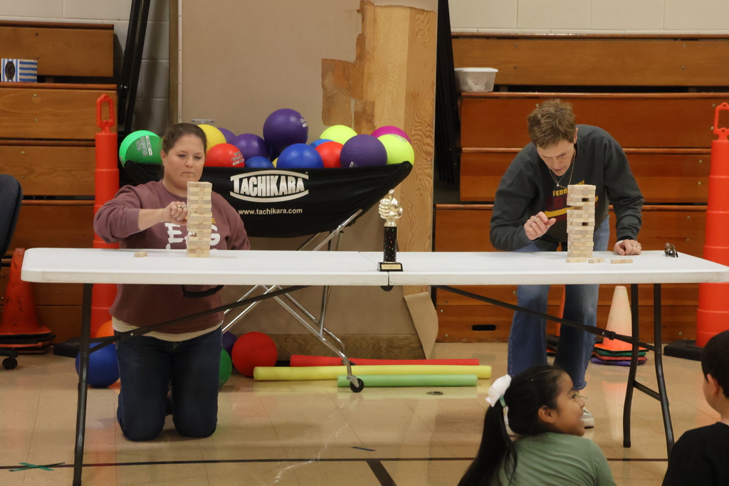 2 teachers compete in a jenga style challenge in the gym