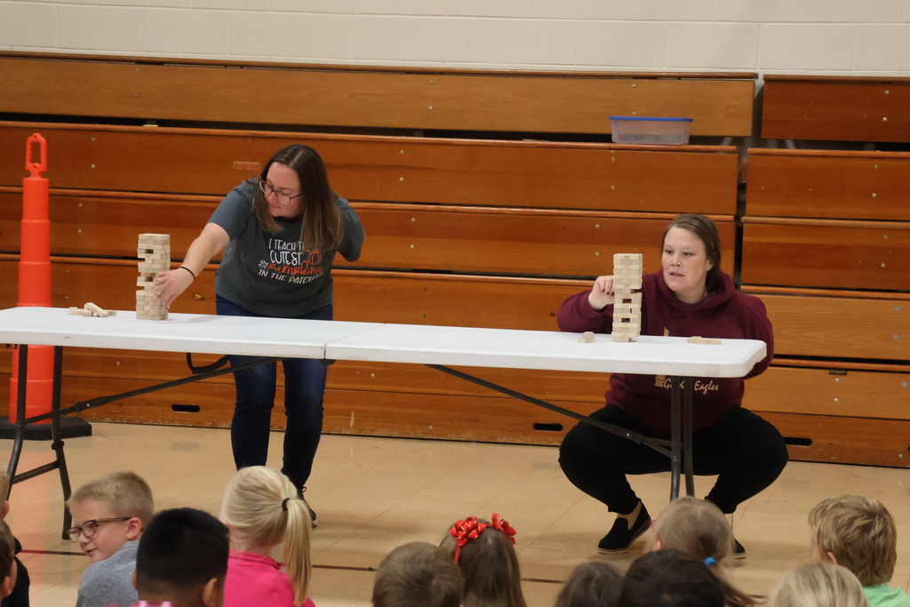 2 teachers compete in a jenga style challenge in the gym