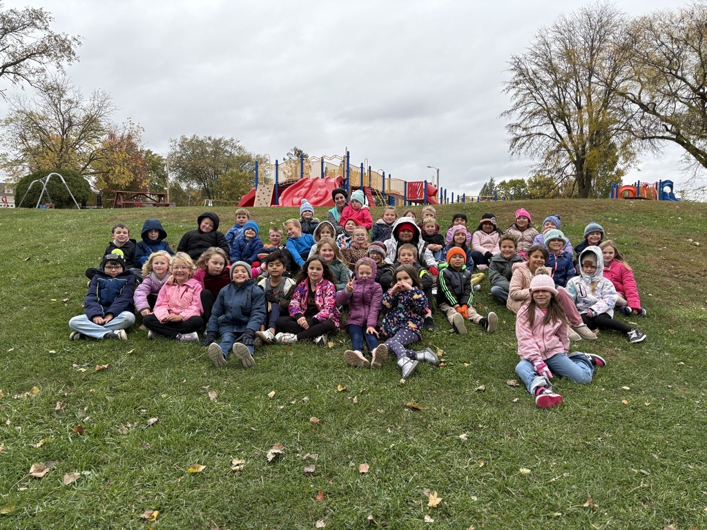 all first graders sit on a hill side at Flora park for a picture