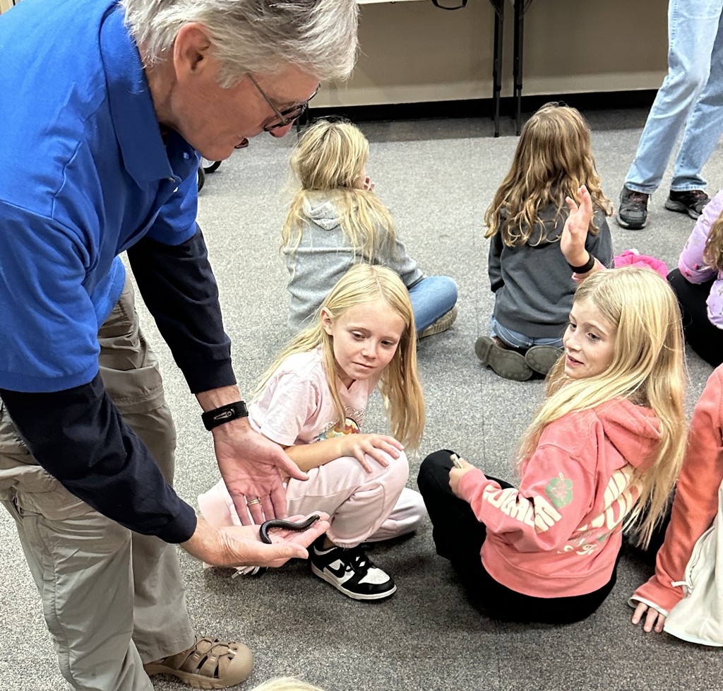 students look at an animal that a guide is holding at the zoo