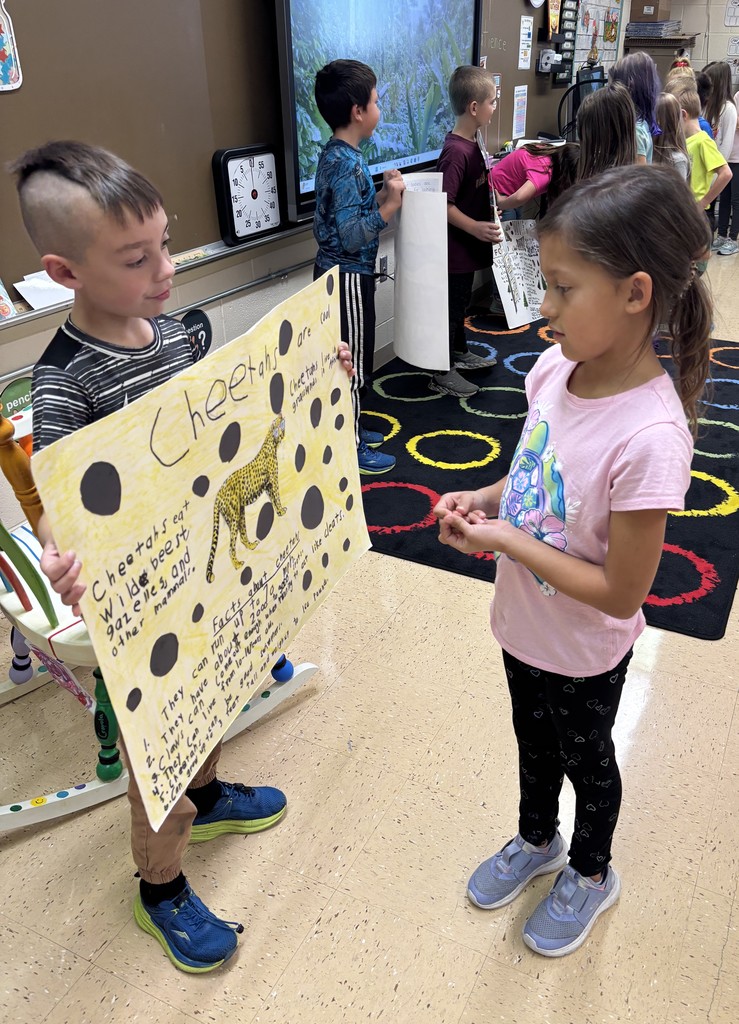 a student shows off their animal poster to a classmate