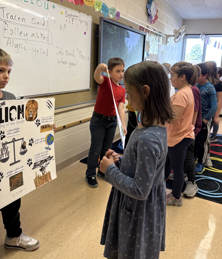 students show off their animal posters to classmates