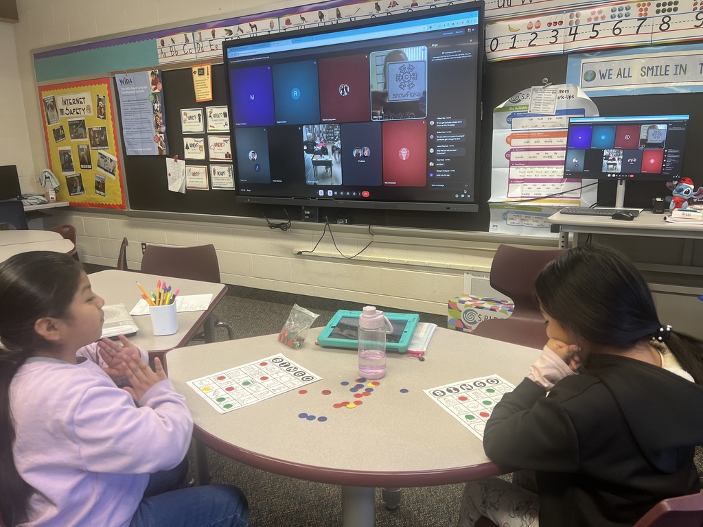 students sit at a table with their bingo cards with zoom meeting showing on screen