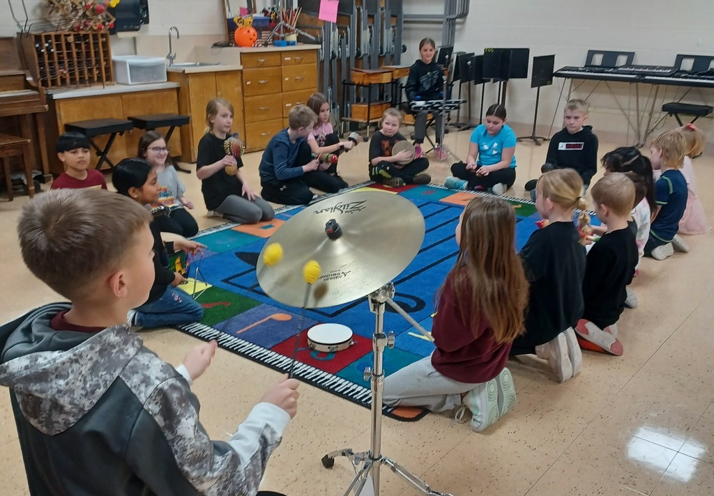 students sit in a circle around a music rug holding different musical instruments