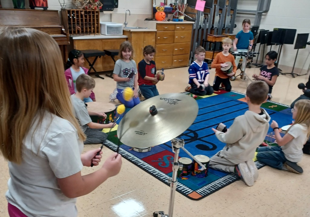 students sit in a circle around a music rug holding different musical instruments
