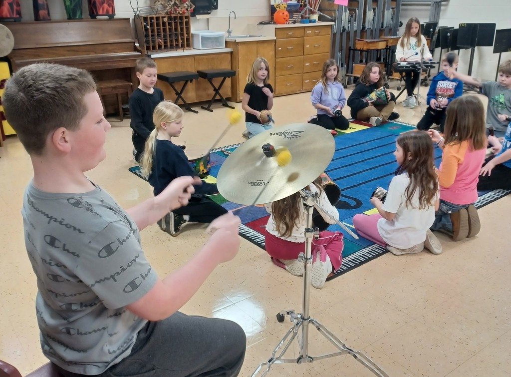 students sit in a circle around a music rug holding different musical instruments