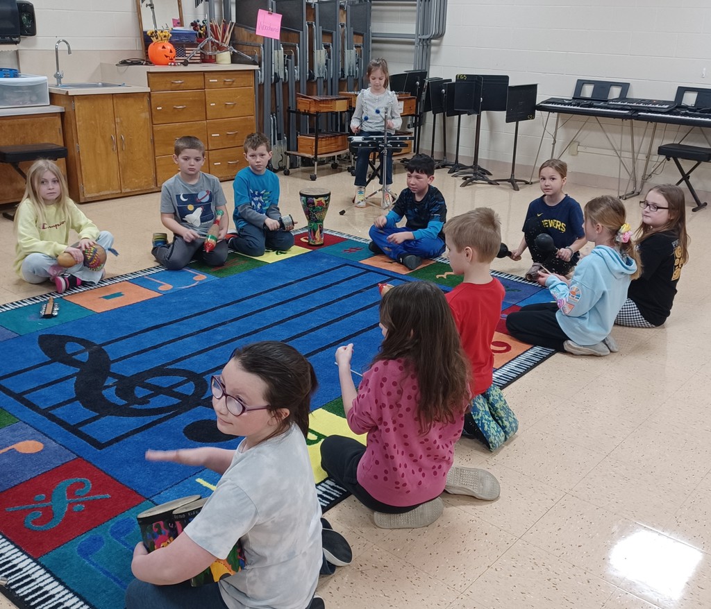 students sit in a circle around a music rug holding different musical instruments
