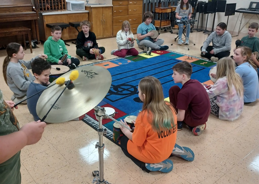 students sit in a circle around a music rug holding different musical instruments