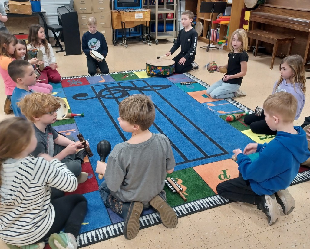 students sit in a circle around a music mug holding different musical instruments