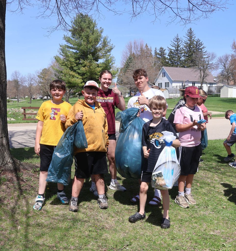 students hold up their trash bags from earth day pick up 