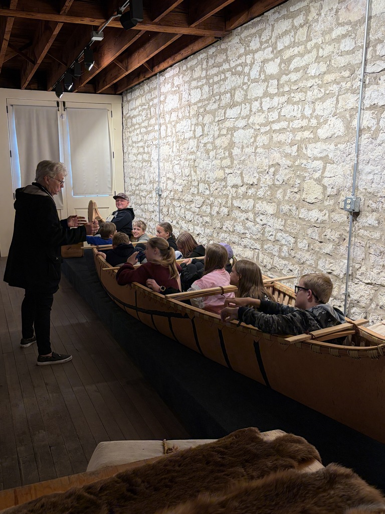 students listen to a speaker as they sit inside a canoe