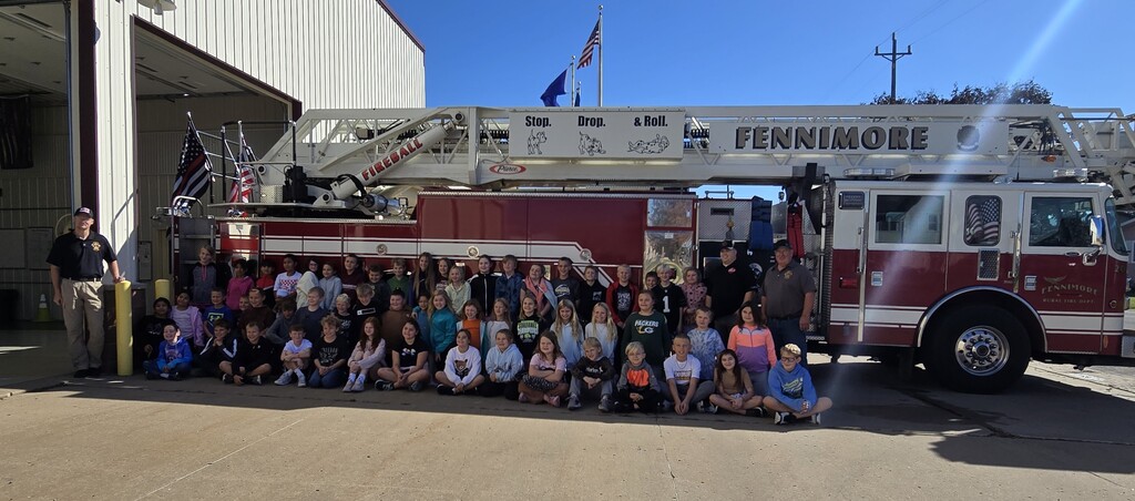 4th grade students pose for a picture with firefighters in front of fire engine