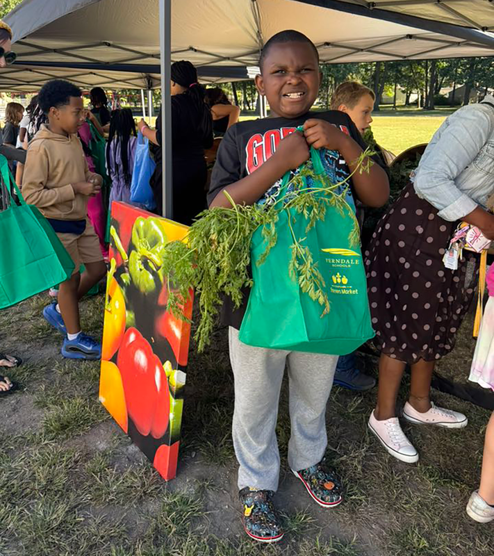 A student holds a heavy bag of fresh produce at FUEL Farmers Market.