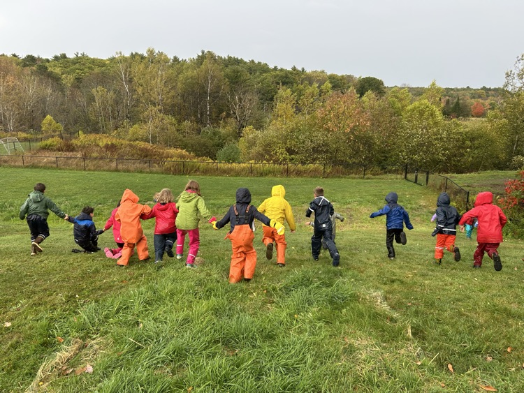 kids in rain gear, running down a grassy hill