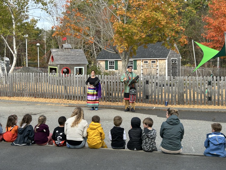 Two Native American performers sing and beat drums for an audience of students and teachers