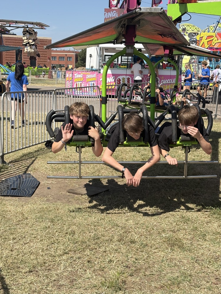 Three band students are strapped into a fair ride in which they are hovering above the ground.