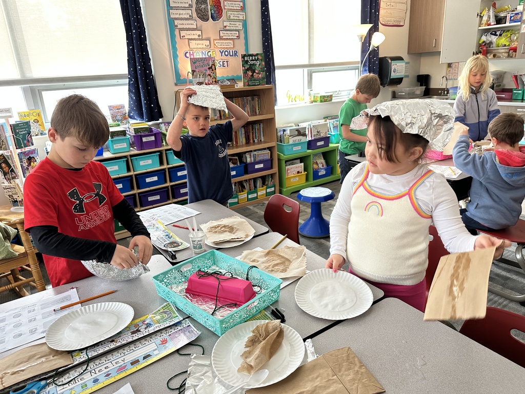 Students designing sun-resistant hats using paper towels, foil, clips, paper plates, and string.