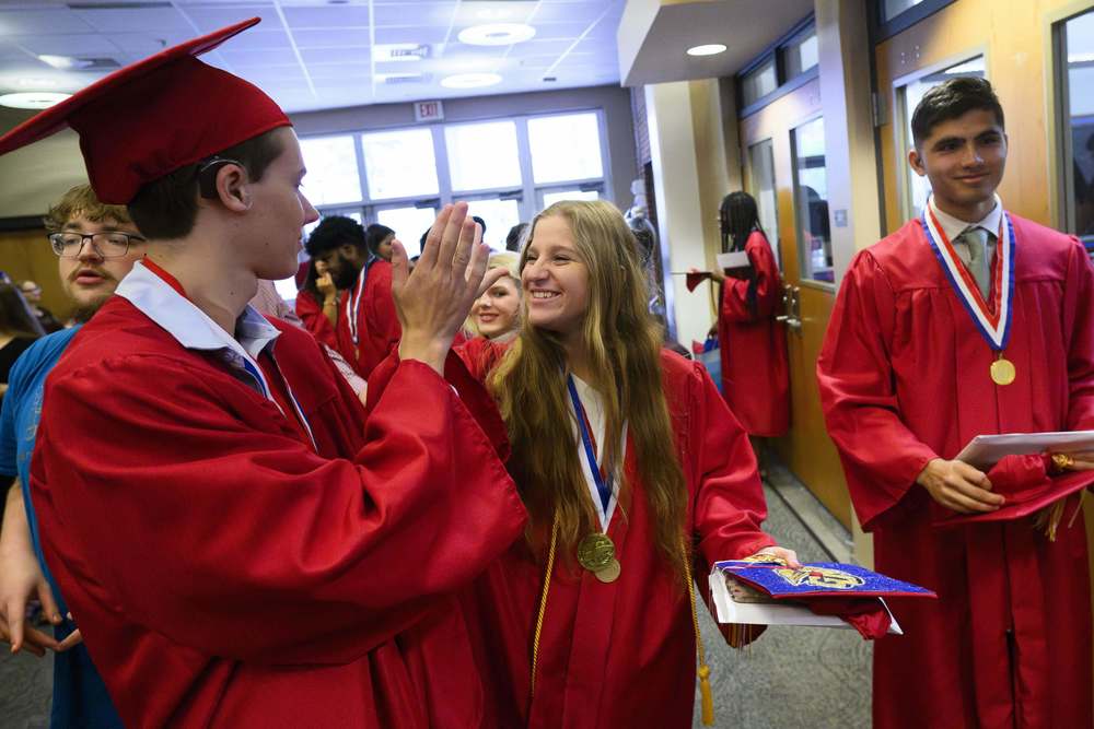 Deaf High School graduates in red cap and gowns high-fiving after graduating.