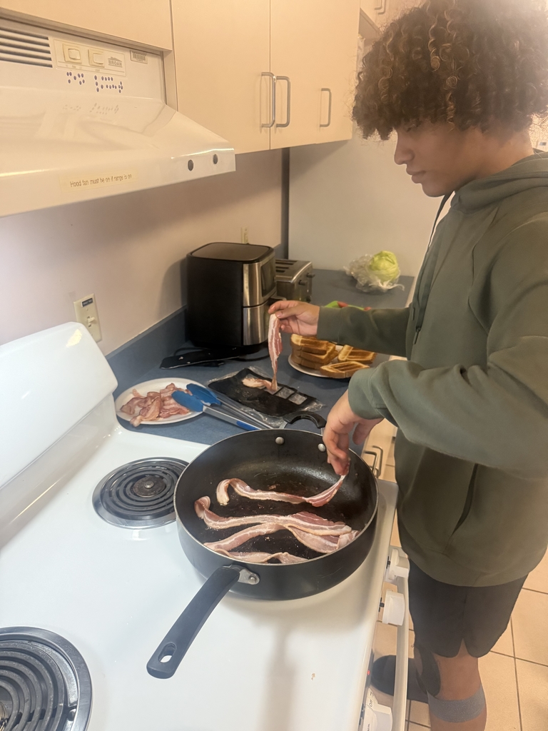 A student is cooking bacon in a pan inside the kitchen in the residential halls.