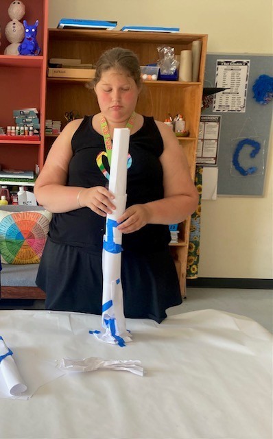 Breanna wraps her hands around her tower assessing its strength and stability. The structure uses a series of paper tubes which are wider at the base and narrower at the top. 