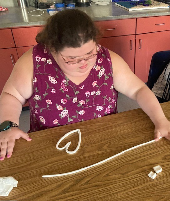 Jessie rolls coils of clay and shapes one into a heart.