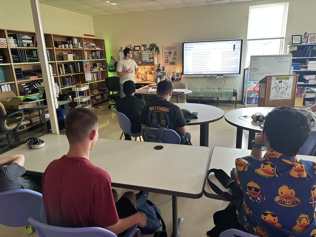 Christes standing at front of classroom reading off Smartboard; students listening at their classroom seats