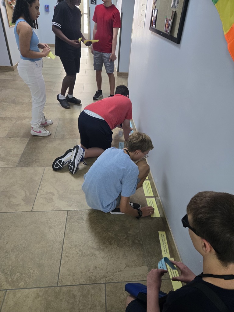 Students building the long timeline of yellow cards along the hallway floor