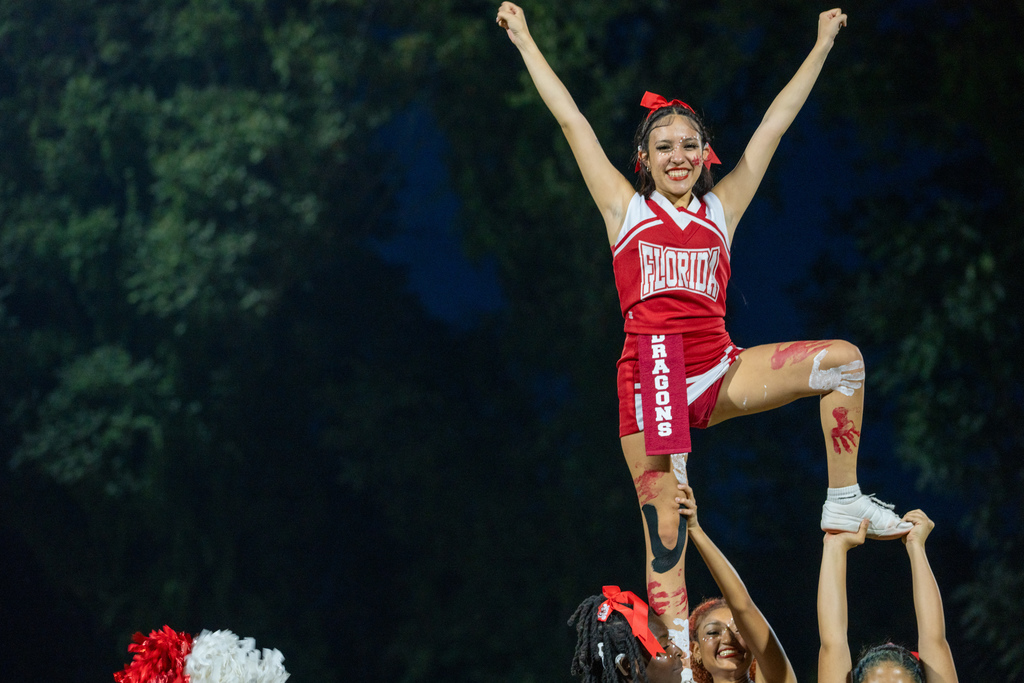A FSDB cheerleader is smiling as she holds her position in a stunt on the field during half time show. 