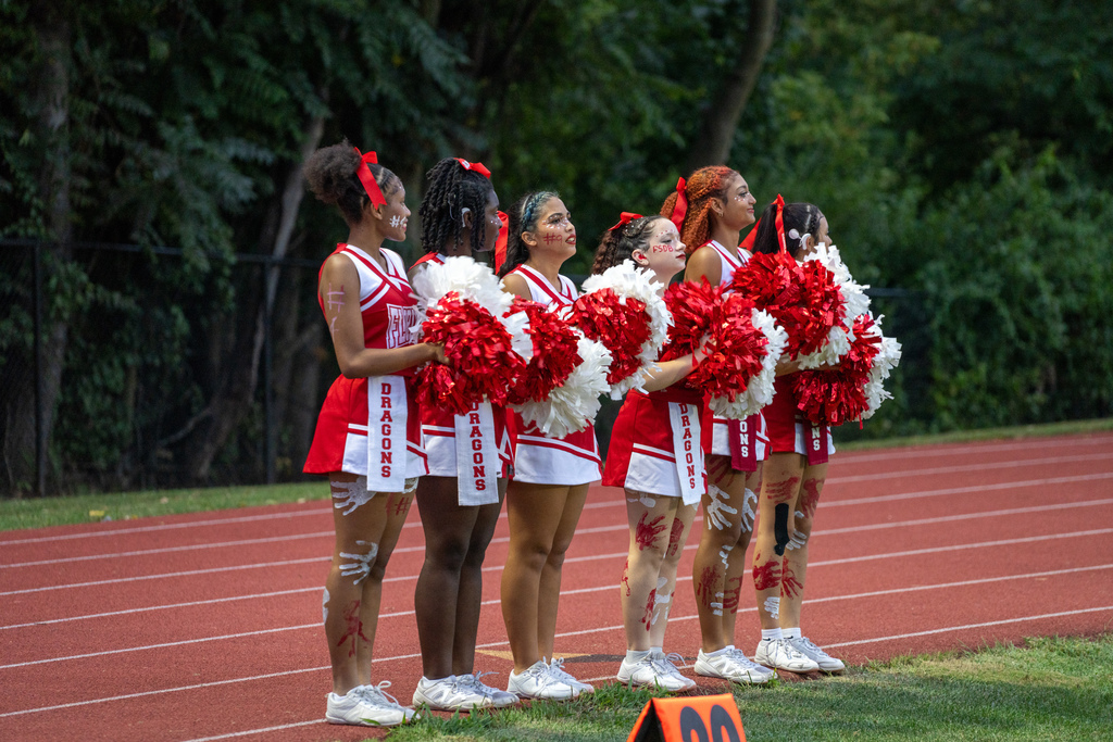 Six FSDB cheerleaders holding red and white pom poms cheering for the boys on the field. 