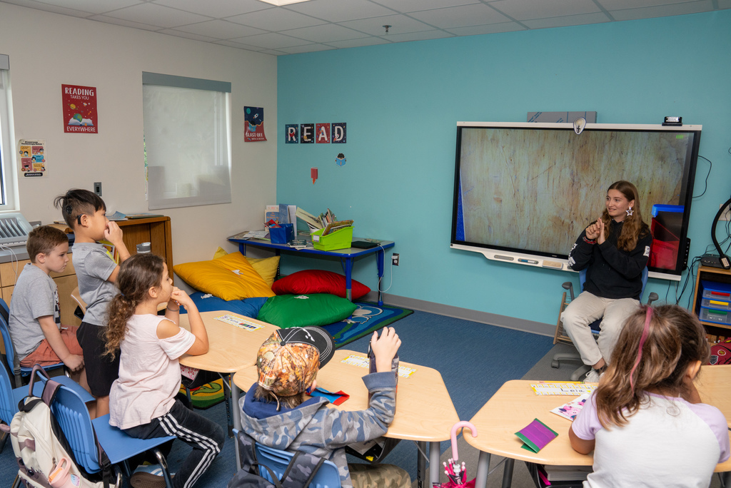 A wide shot of Brenna reading her story to the 2nd grade class.