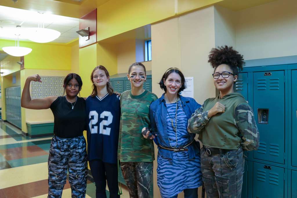 Four students with a staff member dressed in camo and blue Na'vi clothing smile for a photo in the hallway of Pope. 