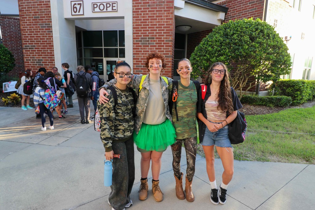 Four students dressed in camo smile for a photo outside of Pope. 
