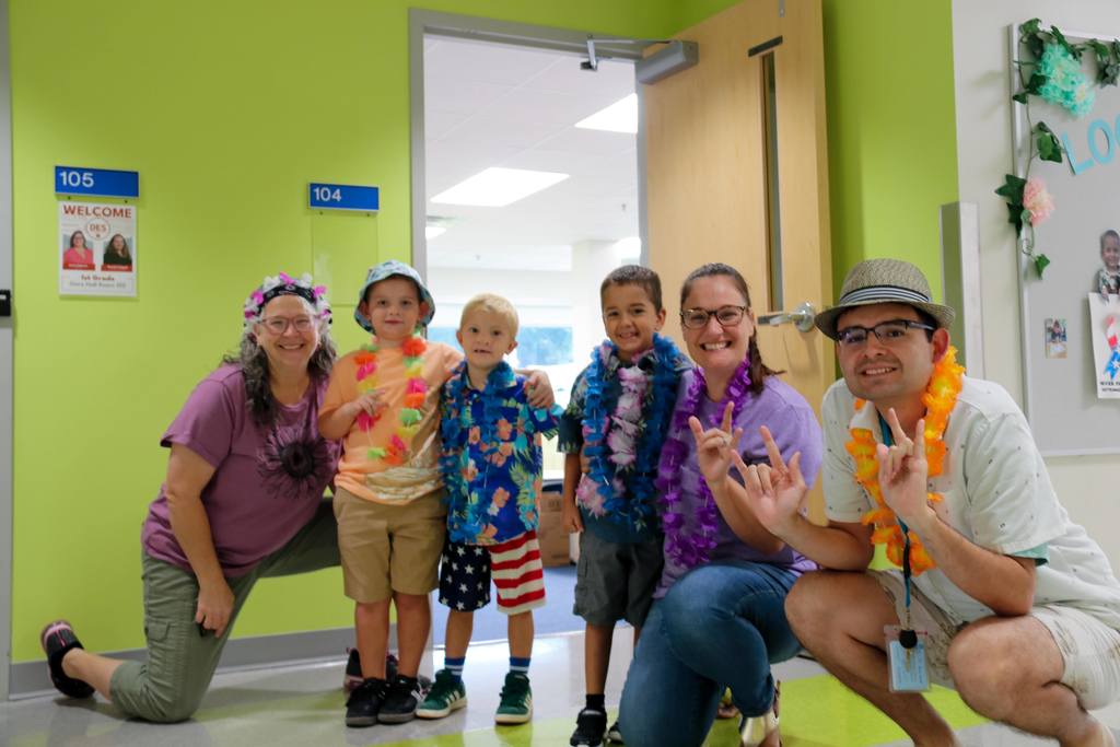 Elementary students smile with their teachers dressed in colorful clothing and Hawaiian leis. 