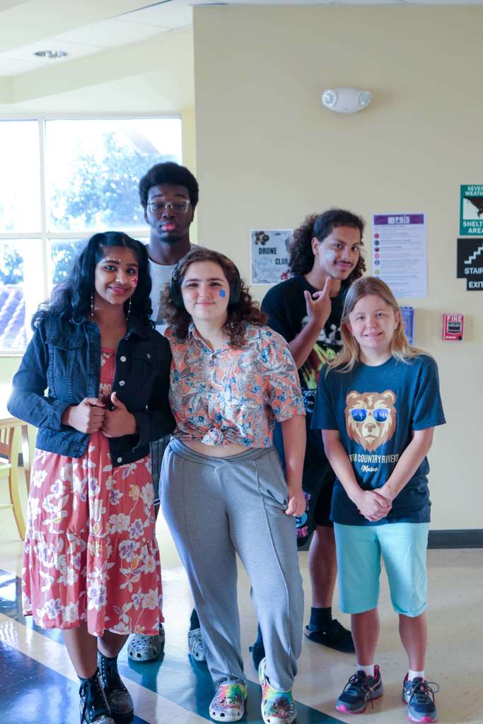 Five students dressed in floral and colorful clothing as they smile for their photo in the hallway of Pope. 