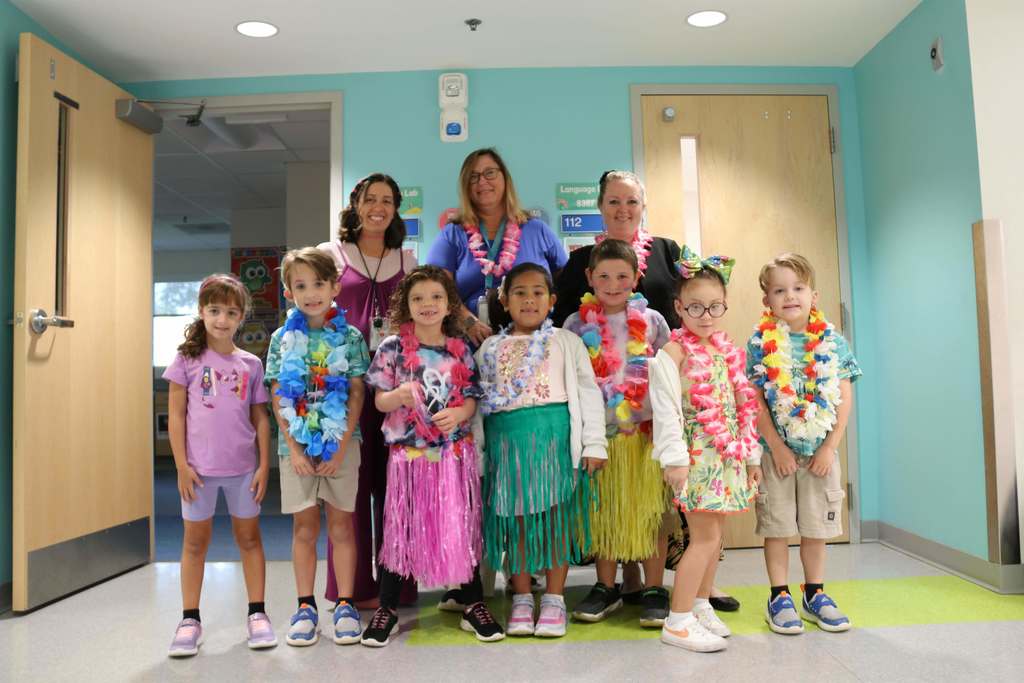 Elementary students wearing colorful Hawaiian skirt and leis smiling with their teachers in the hallway of Gore. 