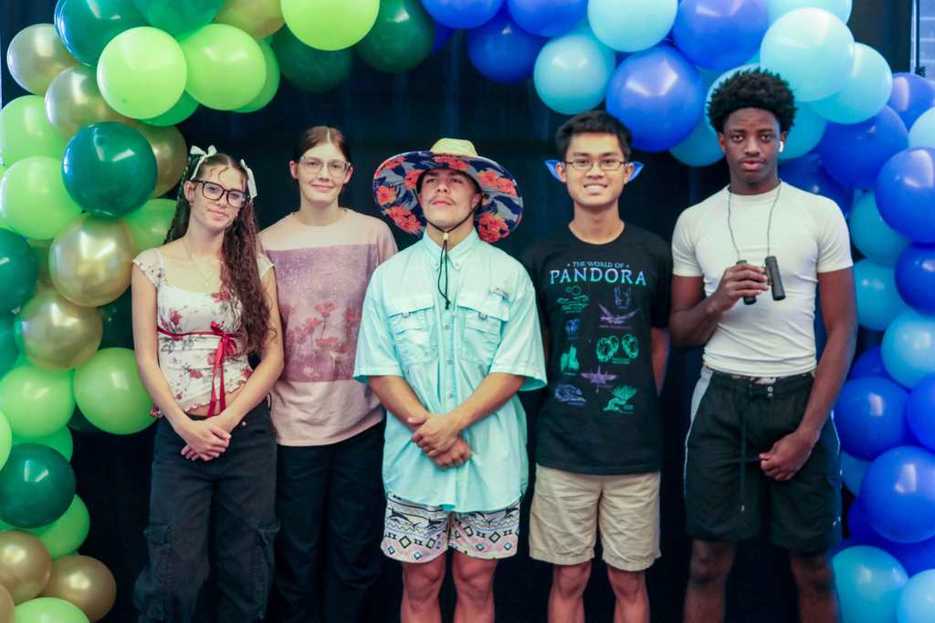 Five students wearing coloful and nature color clothing as they smile for their photo at the photo op booth. 